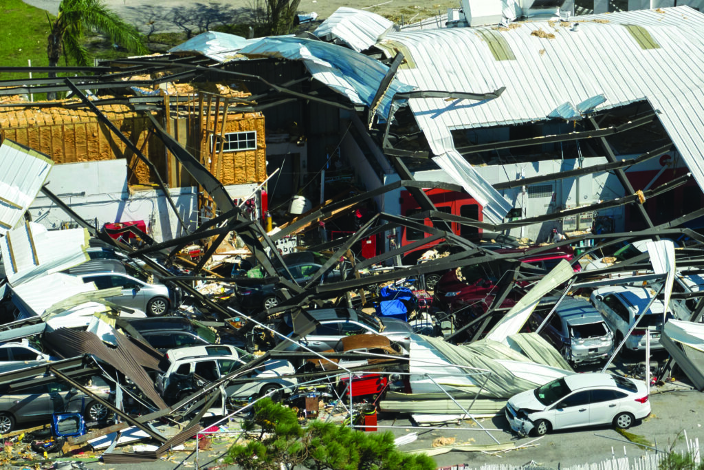 Hurricane Ian destroyed industrial building with damaged cars under ruins in Florida. Natural disaster and its consequences.